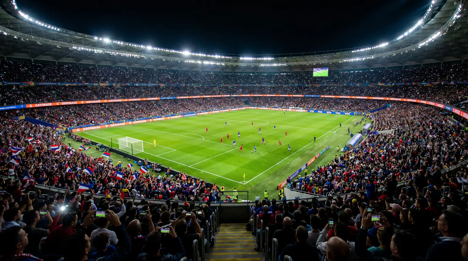 Football stadium at night with live match in progress and dynamic atmosphere under floodlights
