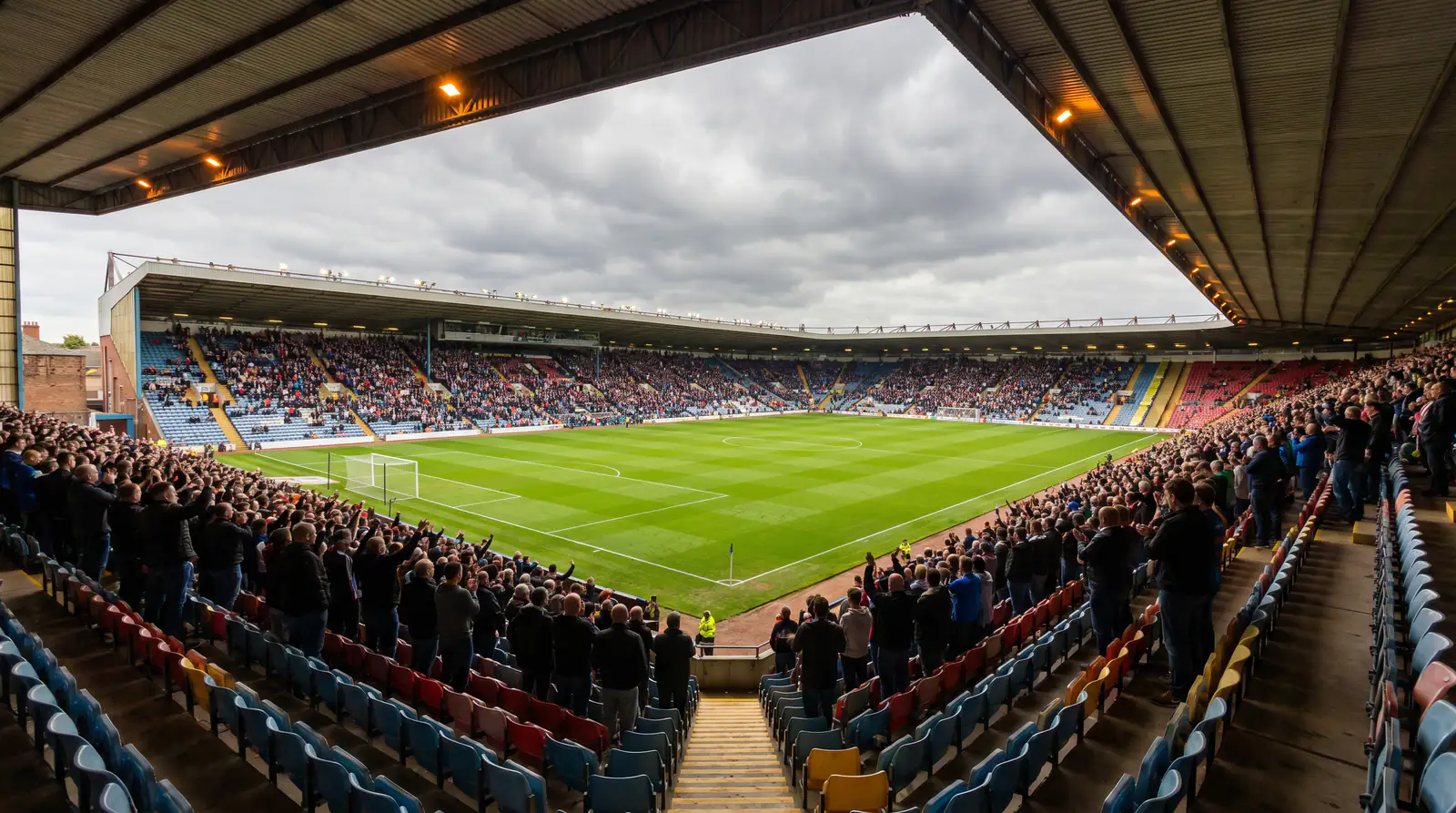 Packed UK football stadium on matchday with floodlights illuminating the pitch